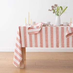 May include: A red and white striped linen tablecloth with a natural, slightly textured weave. The tablecloth is laid out on a wooden table with a vase of flowers and candles.