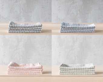 May include: Four stacks of folded linen napkins in four different colors: black and white, blue and white, pink and white, and green and white.