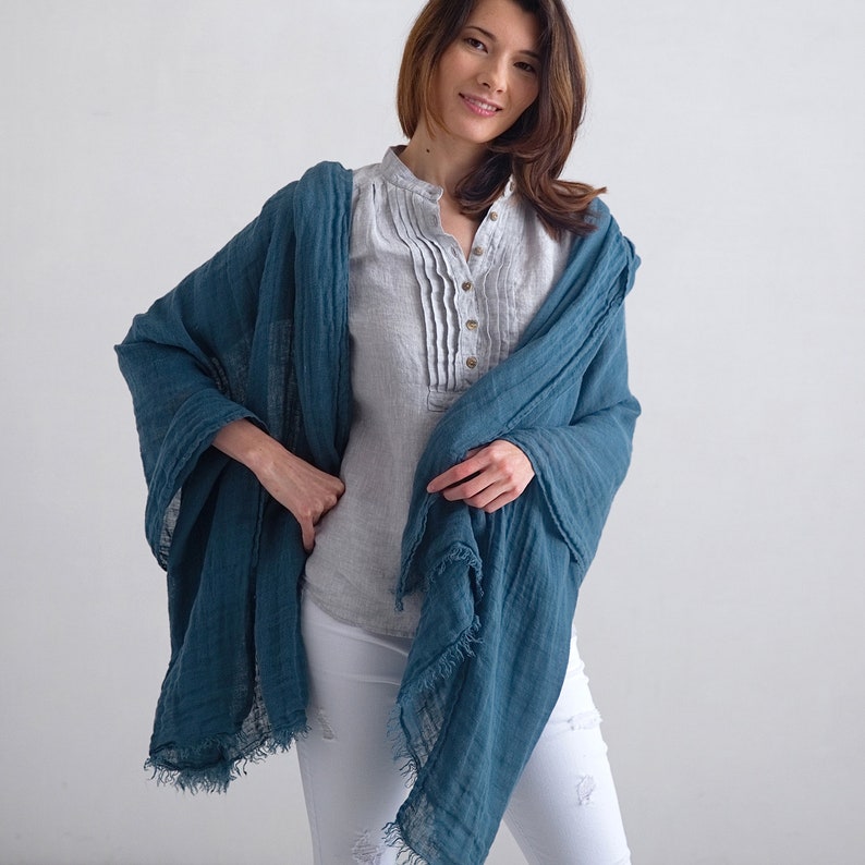 May include: A teal blue linen scarf with frayed edges. The scarf is draped around a person's neck and shoulders.