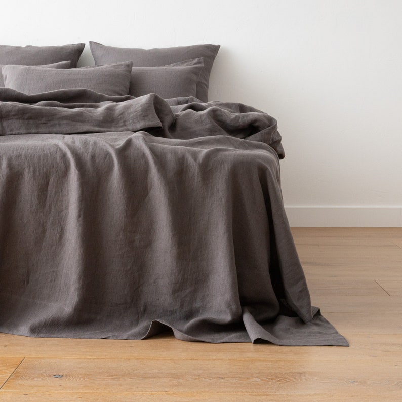 May include: A dark gray linen duvet cover with a smooth, textured surface. The duvet cover is folded and draped over a bed with matching pillowcases.