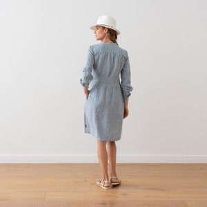 May include: A light blue linen dress with a white hat. The dress has a button-up front and long sleeves.