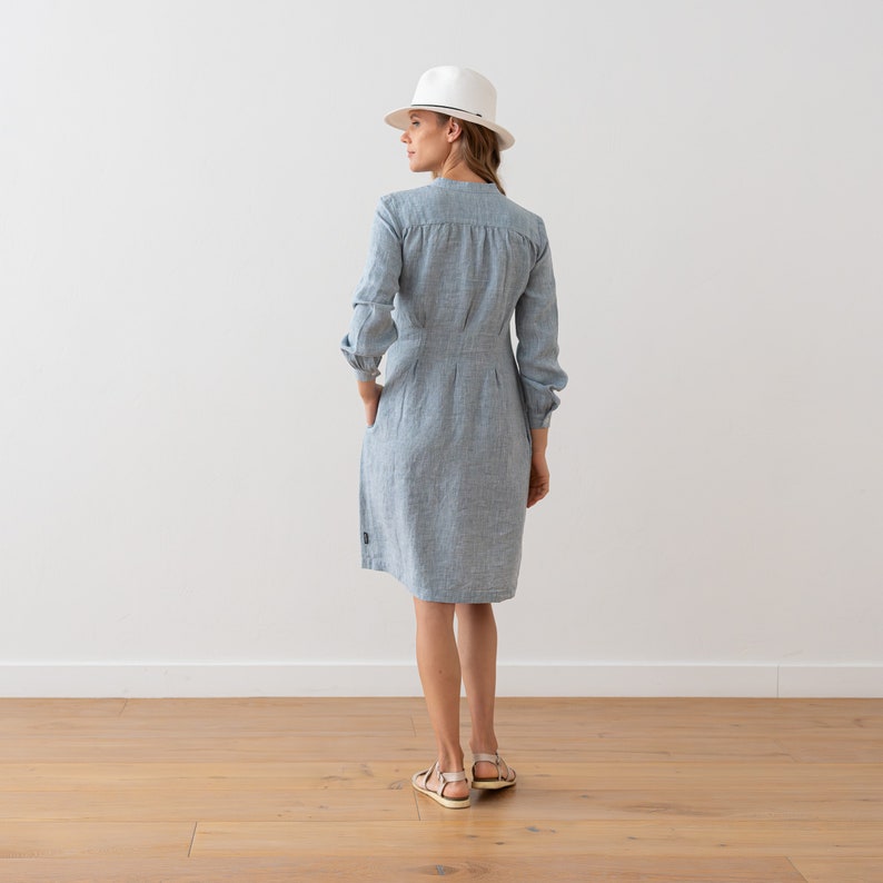 May include: A light blue linen dress with a white hat. The dress has a button-up front and long sleeves.