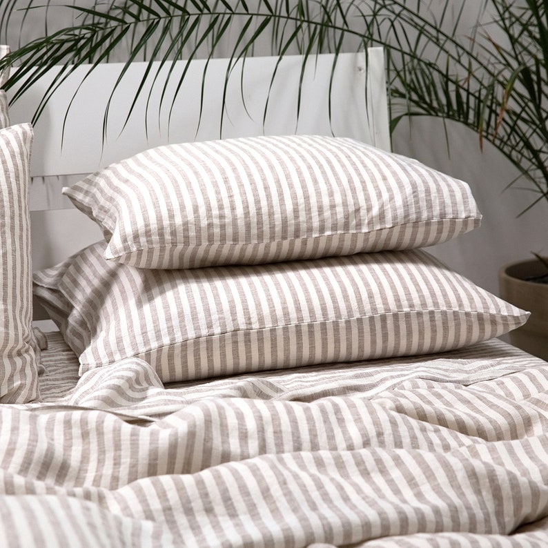 May include: A set of two striped linen pillowcases in a beige and white color scheme. The pillowcases are made of a soft, breathable fabric and are perfect for adding a touch of elegance to any bedroom.