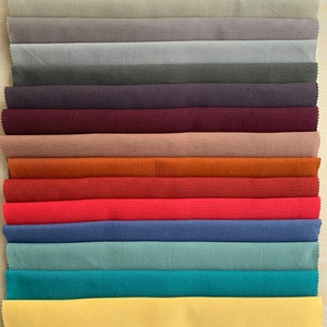 May include: A collection of 14 fabric swatches in various colors, including white, beige, gray, purple, maroon, brown, orange, red, blue, teal, turquoise, yellow, and green. The swatches are arranged in a vertical stack, with the white swatch at the top and the green swatch at the bottom.