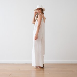 May include: A white linen jumpsuit with thin straps and a wide leg. The model is wearing a white hat and sandals.