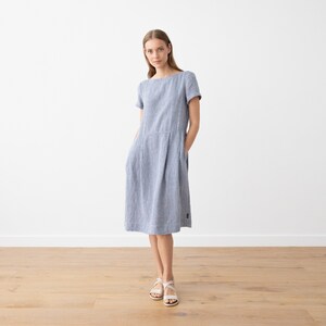 May include: A blue and white striped linen dress with short sleeves and a scoop neck. The dress has pockets on the sides and falls to the knee.