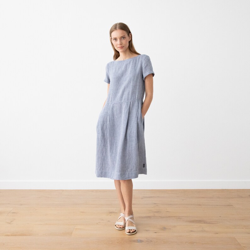 May include: A blue and white striped linen dress with short sleeves and a scoop neck. The dress has pockets on the sides and falls to the knee.