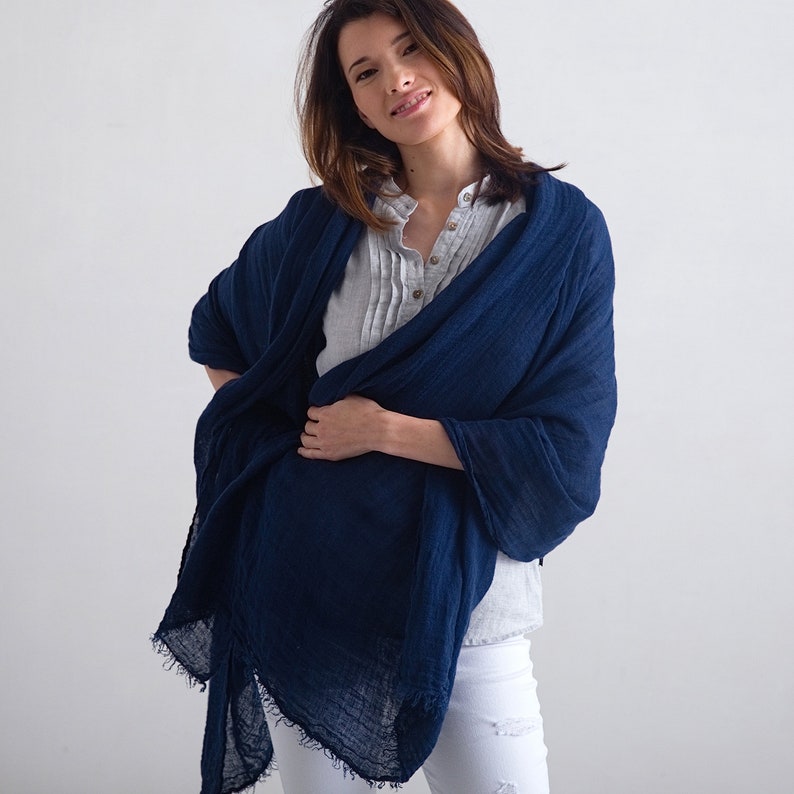 May include: A navy blue linen scarf with a frayed edge. The scarf is draped around a person's neck and shoulders.