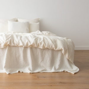 May include: A white linen bed with a white duvet cover and white pillowcases. The bed is made with a white linen bed skirt.
