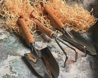 May include: Three gardening tools with polished stainless steel heads and light wood handles. Each handle is engraved with text: Love Louie & Lucie x, Drill the Hearty, and Aunty Charlotte. Each tool features a brown leather hanging loop.