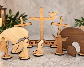 May include: A wooden Easter nativity set featuring three crosses, one with a dove, and the text He Is Risen. The set includes figures of a soldier, an angel, a kneeling person, a standing figure with arms raised, and a tomb with a stone entrance.