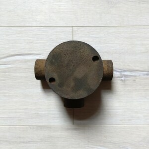 May include: A rusty metal junction box with three openings for electrical wiring. The box is round and has a flat top.