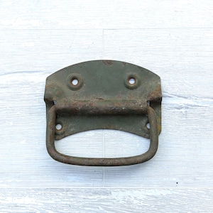 May include: An aged metal handle, olive green in colour with signs of rust. The handle has a curved, arched design with a curved bar for gripping. Two small holes are visible on the top of the handle.