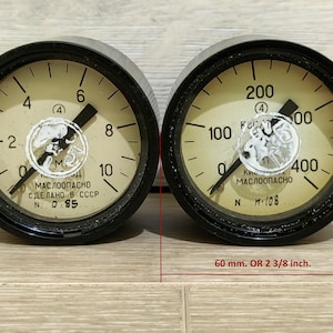 Può includere: Due indicatori analogici rotondi con cornici nere e quadranti bianchi. Gli indicatori hanno aghi neri e marcature nere. L'indicatore sinistro legge da 0 a 10 ed è etichettato "маслоопасно сделано в СССР N 0-85". L'indicatore destro legge da 0 a 400 ed è etichettato "Кисл. маслоопасно N H-108". Gli indicatori hanno un diametro di 60 mm.
