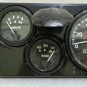May include: A black dashboard with three gauges. The gauges are labeled "MASLO", "BODA", and "km/h". The "MASLO" gauge has a needle pointing to 4, the "BODA" gauge has a needle pointing to 80, and the "km/h" gauge has a needle pointing to 0. The "km/h" gauge also has a digital display that reads 00000.