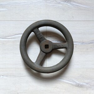 Könnte beinhalten: Ein großes, rundes, graues Gusseisenrad mit drei Speichen. Das Rad hat ein quadratisches Loch in der Mitte und den Text "CSN" und "PUD" auf der Felge.