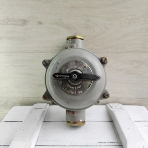 May include: A gray metal electrical switch with a black lever. The switch has a round face with the text "UBS 50 MI 665" and "220V 40A" printed on it.