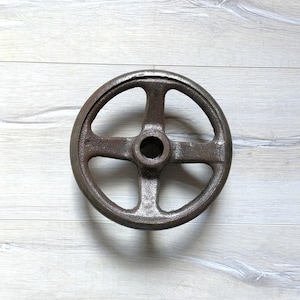 Könnte beinhalten: Ein rostiges Metallrad mit fünf Speichen und einem zentralen Loch. Das Rad ist kreisförmig und hat einen Durchmesser von etwa 25 cm.