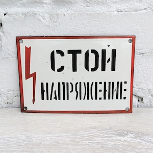 Peut inclure: Panneau rectangulaire en métal blanc avec un bord rouge et un éclair rouge sur le côté gauche. Le panneau porte le texte noir en pochoir "СТОЙ НАПРЯЖЕНИЕ".