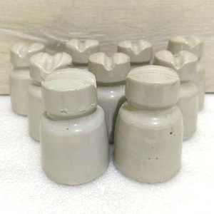 May include: A group of ten white ceramic insulators with a textured surface. The insulators are arranged in a circle with the tops facing up.