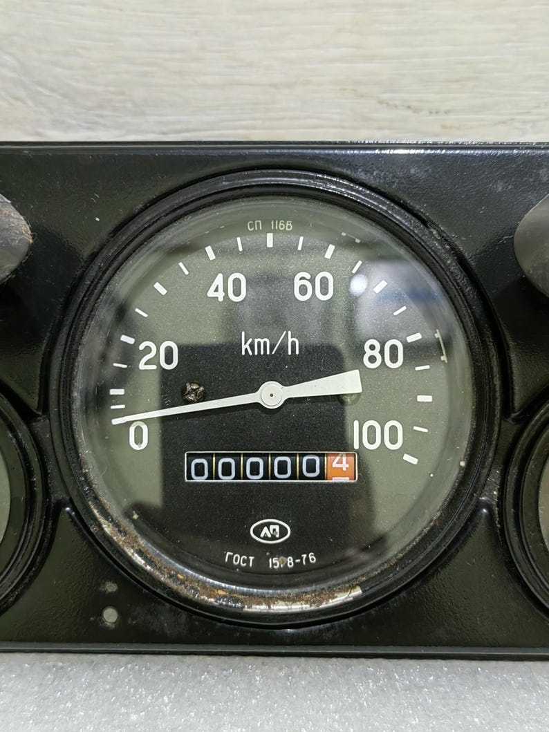 May include: A black dashboard with a speedometer that reads 000004 km/h. The speedometer has a white needle and a black face with white markings. The text "СП 1168" and "ГОСТ 1598-76" are visible on the face of the speedometer.