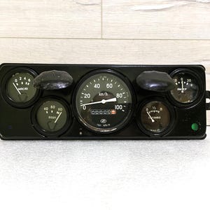 May include: A black dashboard with six round gauges, including a speedometer that reads up to 100 km/h. The gauges are labeled with numbers and text, including "km/h", "00000", and "1/2".