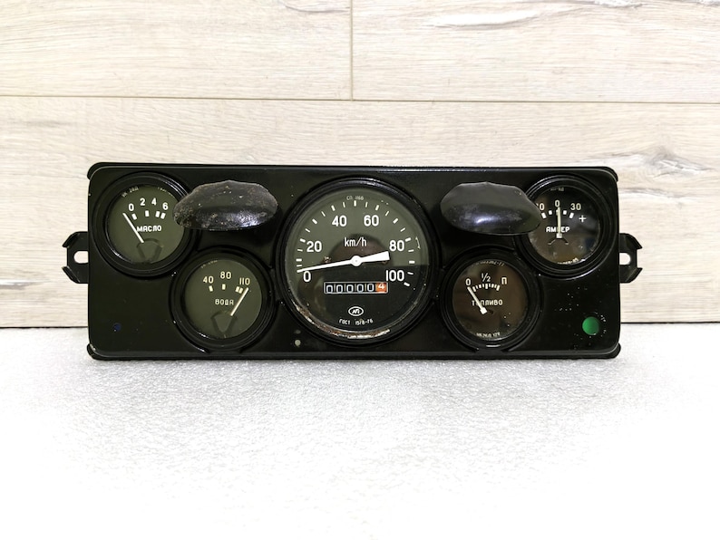 May include: A black dashboard with six round gauges, including a speedometer that reads up to 100 km/h. The gauges are labeled with numbers and text, including "km/h", "00000", and "1/2".