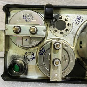 May include: Close-up of the back of a vintage gauge with a green lens, two metal plates with screws, and markings that read "СССР" and "09-68".