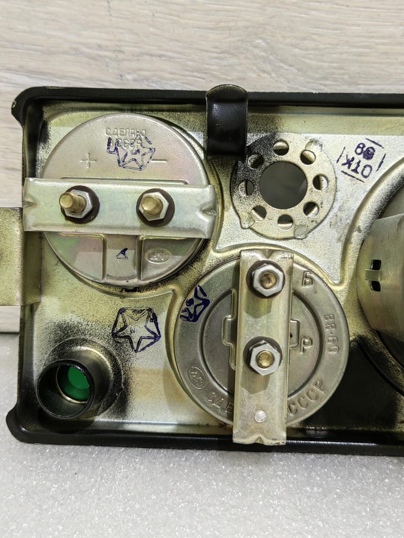 May include: Close-up of the back of a vintage gauge with a green lens, two metal plates with screws, and markings that read "СССР" and "09-68".