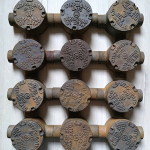 May include: Nine rusty metal electrical junction boxes with lids. Each lid has the text "ОТКРЫВАТЬ В475" and "ОТКЛЮЧИВ ОТ СЕТИ" in Cyrillic script. The boxes are arranged in three rows of three.
