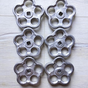 Puede incluir: Seis pomos de metal plateado de estilo industrial con seis agujeros cada uno. Los pomos tienen forma de estrella con un cuadrado en el centro.