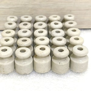 May include: A collection of 20 white ceramic electrical insulators. The insulators are cylindrical with a hole in the center. They are arranged in a rectangular pattern.