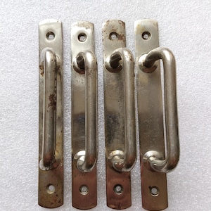 May include: Four silver metal door handles with a rounded rectangular shape and a curved handle. The handles have a slightly worn, aged look.