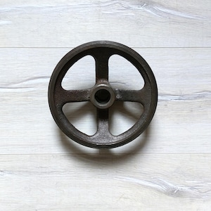Könnte beinhalten: Ein Gusseisenrad mit vier Speichen und einem zentralen Loch. Das Rad ist dunkelbraun und hat ein rustikales Aussehen.