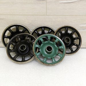 Pode incluir: Cinco rodas de metal com um design decorativo. Quatro das rodas são pretas com uma borda prateada e uma é verde com uma borda prateada.