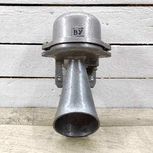 Puede incluir: Una bocina metálica vintage de estilo industrial, pintada en gris mate. La bocina presenta una abertura en forma de campana y una parte superior cilíndrica con las letras "BY". Está montada en una pared.