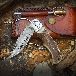 May include: A personalized folding knife with a patterned blade and a handle made of brown material. The blade has the text "Love You" etched on it. The knife is next to a brown leather case with a key ring.