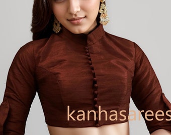 May include: A dark brown blouse with a high mandarin collar, three-quarter length sleeves, and a front button placket featuring small fabric-covered buttons. The garment has a textured finish and displays the text kanhasarees in the center.