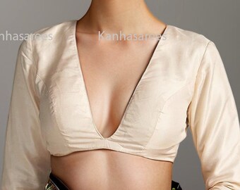 May include: A cream-colored, long-sleeved blouse with a deep V-neckline. The blouse is made of a soft, silky fabric and has a fitted silhouette.