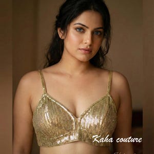 May include: A gold sequined top with thin straps. The top has a V-neck design and is embellished with small, shiny sequins. The text "Kaha couture" is visible on the bottom right of the image.