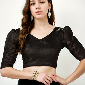 Peut inclure: Un chemisier noir court à col en V et manches bouffantes. Le chemisier est en tissu brillant et a une silhouette ajustée.