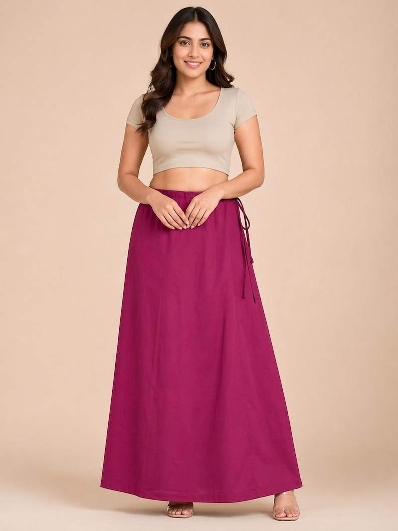 May include: A woman wearing a beige crop top and a long, flowing magenta skirt. The skirt is tied at the waist with a matching drawstring. The outfit is simple and elegant, suitable for various occasions.