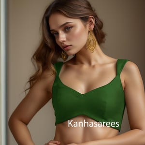 May include: A sleeveless, dark green top with a V-neckline. The text "Kanhasarees" is printed in white across the front. The model is wearing gold earrings.