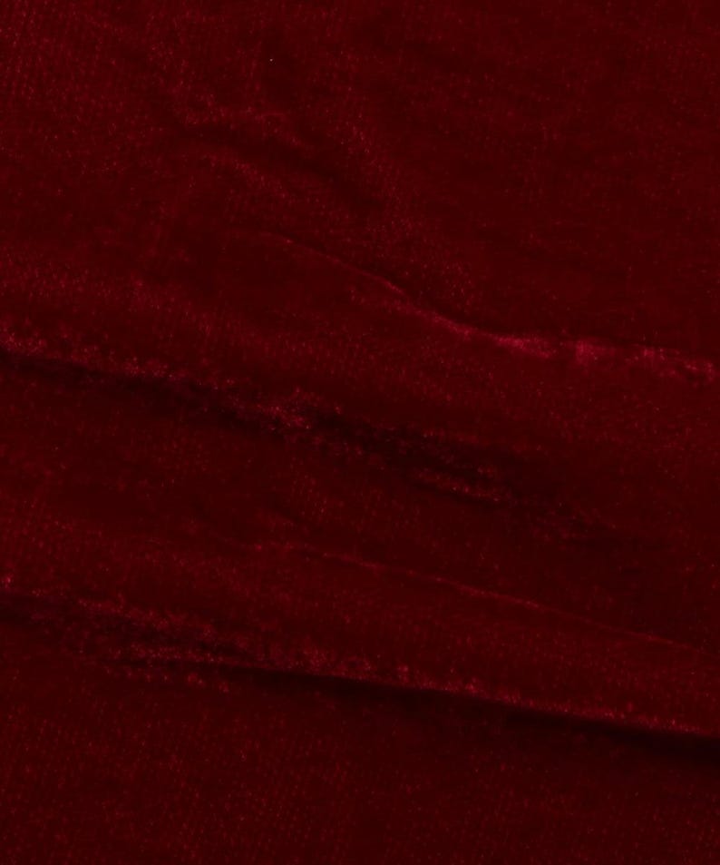 May include: Close-up of a deep red velvet fabric with a soft, plush texture. The fabric is slightly wrinkled, creating a subtle pattern.