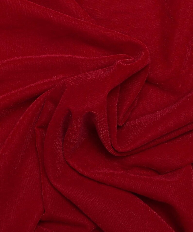 May include: Close-up of a deep red velvet fabric with soft, flowing folds. The fabric has a smooth, luxurious texture.