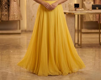 May include: A flowing, bright yellow skirt. The skirt is made of a lightweight fabric that drapes elegantly. The skirt is a solid color and appears to be part of a formal outfit. The skirt is floor-length.