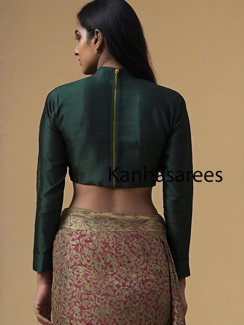 May include: A dark green, long-sleeved, cropped blouse with a gold zipper down the back. The blouse is worn over a red and gold patterned skirt.