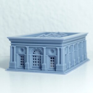 K&ouml;nnte beinhalten: Ein graues 3D-gedrucktes Modell eines Geb&auml;udes im klassischen Stil. Das Geb&auml;ude hat einen rechteckigen Sockel mit einem Satteldach und eine Reihe von S&auml;ulen entlang der Vorderfassade. An der Vorderseite des Geb&auml;udes befinden sich Fenster und T&uuml;ren.