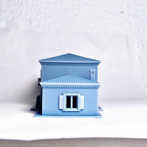 Pu&ograve; includere: Una casa modello di colore azzurro chiaro con una finestra bianca e un piccolo camino. Il modello &egrave; in plastica e misura circa 25 cm di altezza.