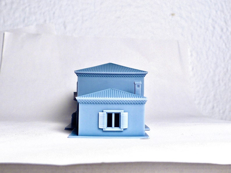 Pu&ograve; includere: Una casa modello di colore azzurro chiaro con una finestra bianca e un piccolo camino. Il modello &egrave; in plastica e misura circa 25 cm di altezza.